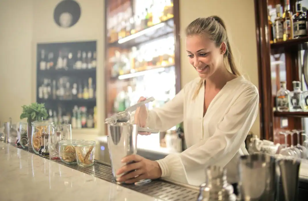 A woman making a cocktail behind the bar.