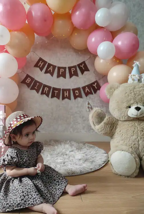 baby sitting on floor in front of birthday banner and balloon arch